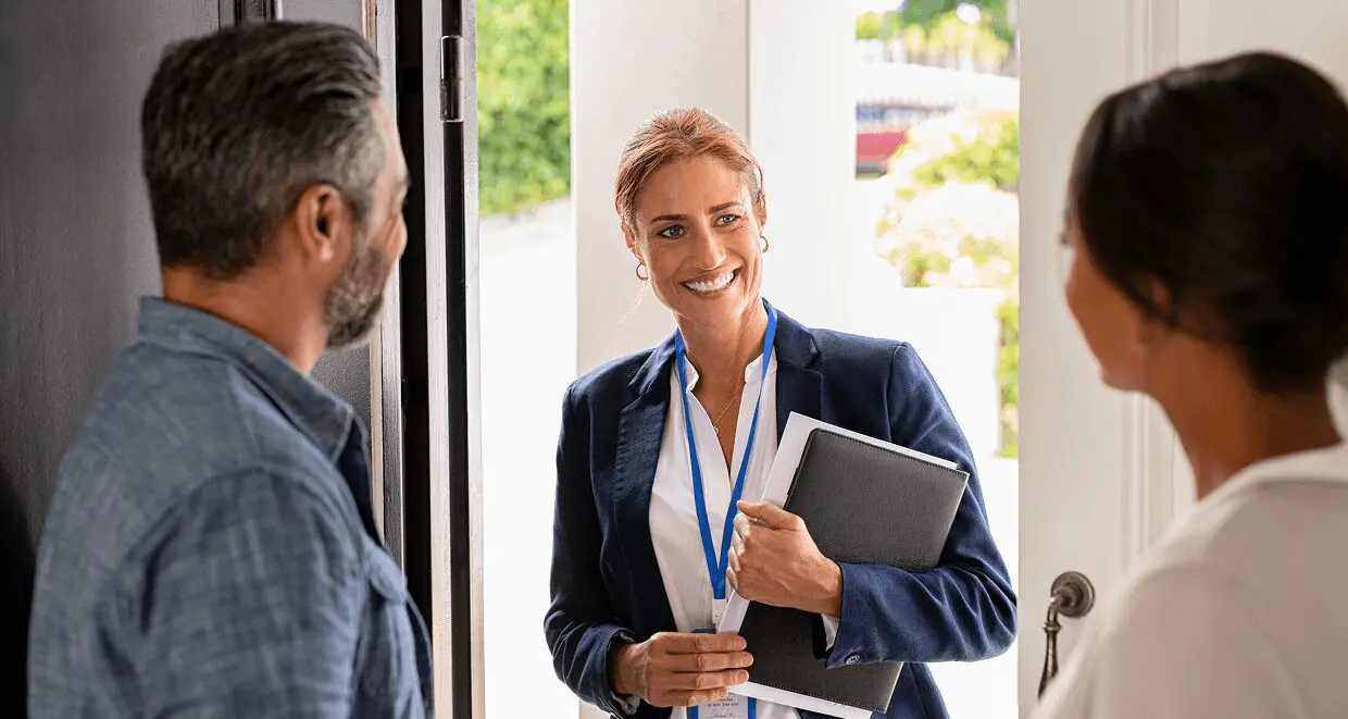 Smiling woman with folder greeting couple indoors.